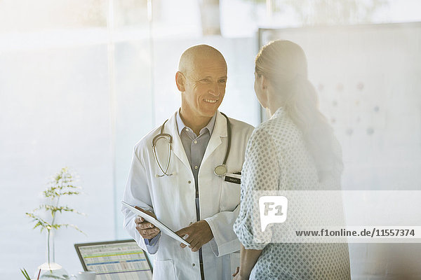 Lächelnder männlicher Arzt zeigt einer Patientin in der Arztpraxis ein digitales Tablet