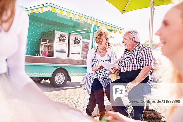 Smiling senior business owners using digital tablet outside food cart