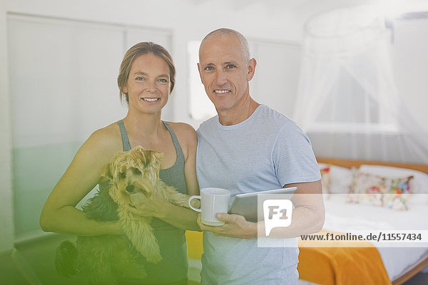 Portrait lächelndes reifes Paar mit Hund und digitalem Tablet im Schlafzimmer