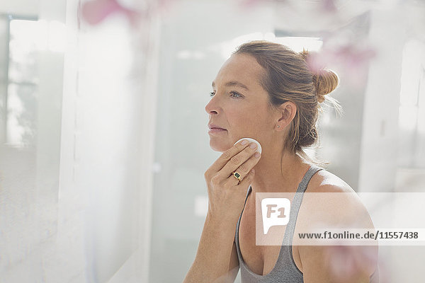 Mature woman applying makeup in bathroom mirror