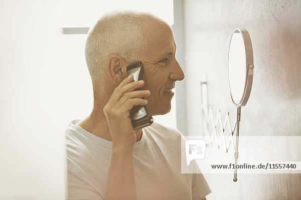 Älterer Mann rasiert sich mit elektrischem Rasierapparat vor einem Vergrößerungsspiegel im Badezimmer
