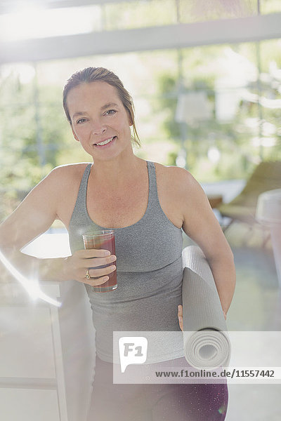 Porträt lächelnde reife Frau mit Yogamatte trinkt Saft Smoothie