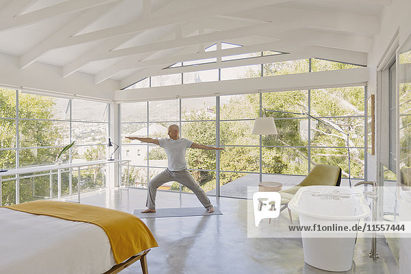 Älterer Mann übt Yoga Krieger 2 Pose in Luxus-Schlafzimmer