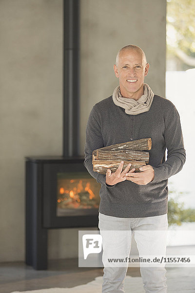 Porträt lächelnd reifen Mann hält Brennholz vor Holz brennenden Kamin