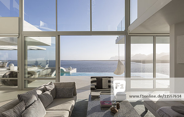 Sunny  tranquil modern luxury home showcase interior living room with patio and ocean view