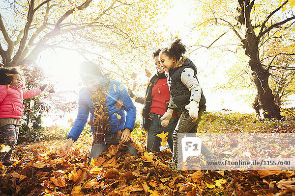 Verspielte junge Familie beim Spielen im Herbstlaub im sonnigen Park