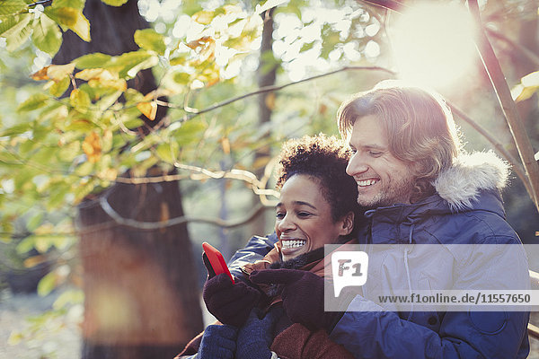 Lächelndes Paar mit Handy im sonnigen Herbstpark