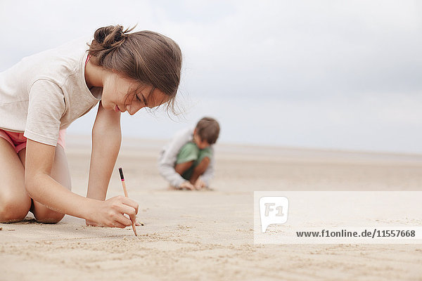 Mädchen mit Stock schreibt im Sand am Sommerstrand