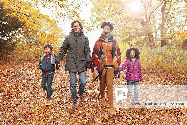 Porträt einer lächelnden jungen Familie  die sich an den Händen hält und den Weg im Herbstpark geht.