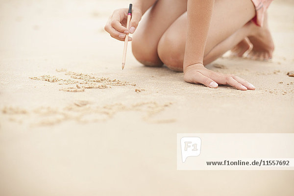 Mädchen mit Bleistift schreibt im Sand am Sommerstrand