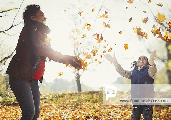Verspielte Mutter und Tochter beim Herbstlaubwerfen im sonnigen Park