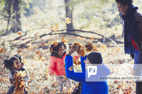 Verspielter Vater und Töchter werfen Herbstlaub in sonnigen Wäldern