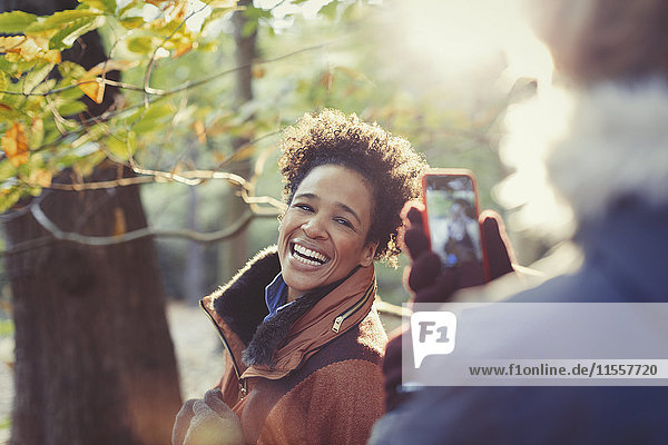 Lächelnde Frau posiert für Freund mit Fotohandy im sonnigen Herbstwald