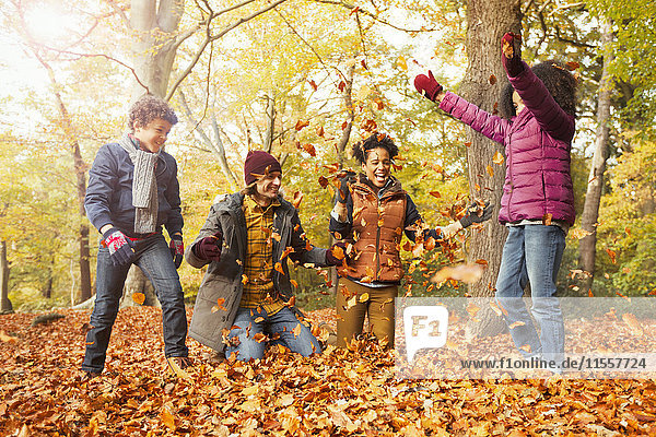 Verspielte junge Familie beim Laubwerfen im Herbstwald