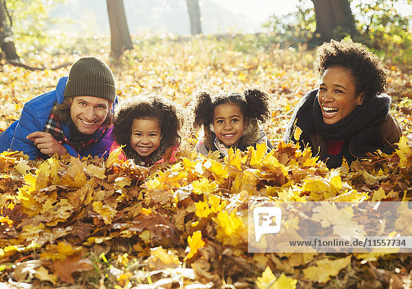 Portrait lächelnde junge Familie im Herbstlaub in sonnigen Wäldern liegend
