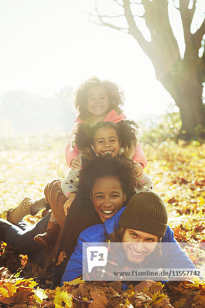 Portrait lächelnde junge Familie in sonnigen Herbstblättern übereinander liegend
