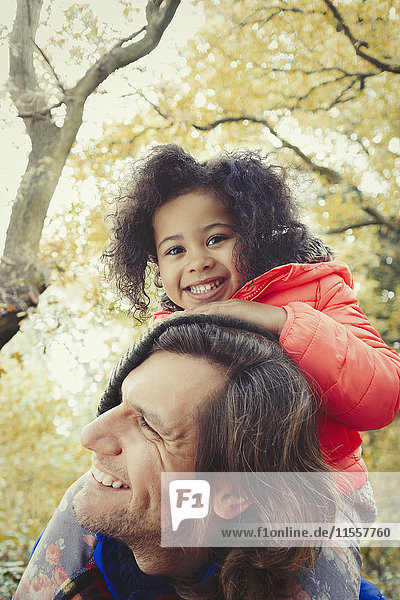 Portrait lächelnder Vater Vater mit Tochter auf Schultern im Herbstpark