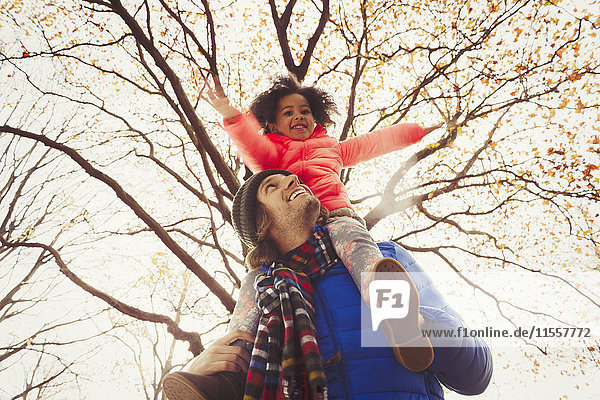 Vater trägt Tochter auf Schultern unter Baum im Herbstpark
