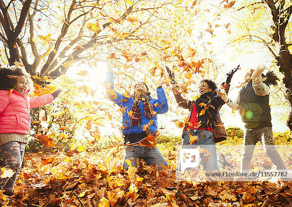 Verspielte junge Familie beim Herbstlaubwerfen im sonnigen Park