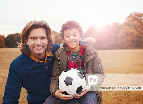 Portrait lächelnder Vater und Sohn mit Fußball im Parkgras