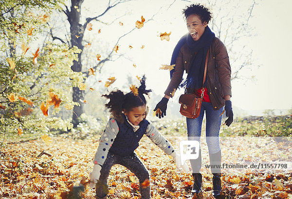Verspielte Mutter und Tochter beim Herbstlaubwerfen im sonnigen Park