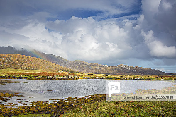 Ruhiger Blick auf Wolken und Regenbogen über sanfte Hügel jenseits des Sees Loch Aineort South Uist Outer Hebrides
