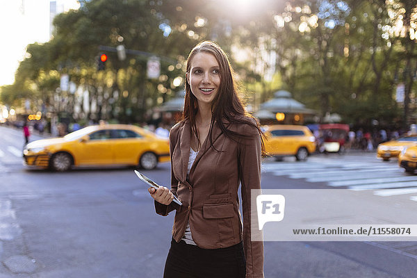 USA  New York  Manhattan  Portrait einer lächelnden jungen Geschäftsfrau mit Tablette auf der Straße