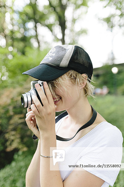 Junge Frau mit einer Vintage-Kamera beim Fotografieren im Park