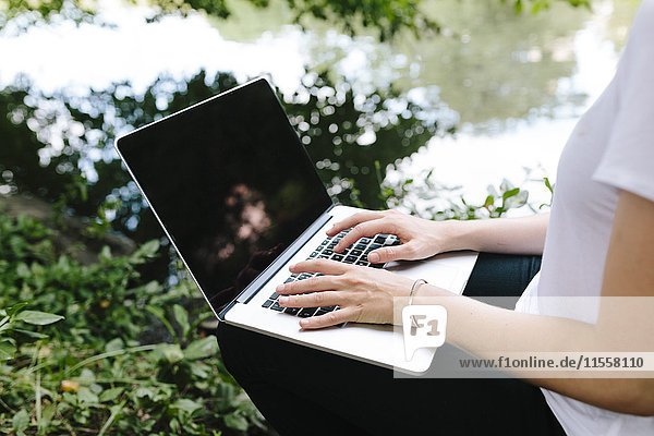 Nahaufnahme der Frau am Seeufer im Park mit Laptop