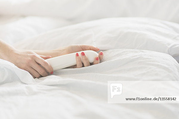 Hand der Frau mit Sexspielzeug im Bett