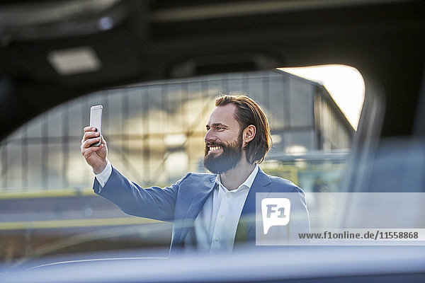 Lächelnder Geschäftsmann mit einem Selfie außerhalb des Autos