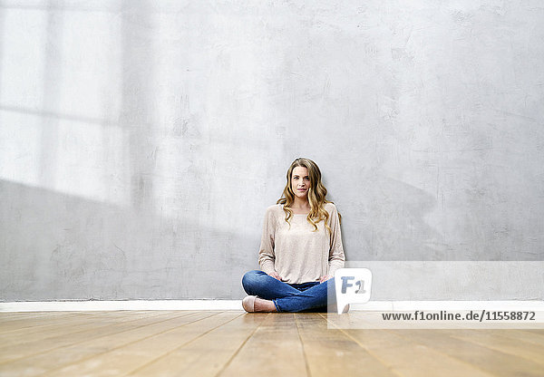 Blond woman sitting on the floor in front of grey wall