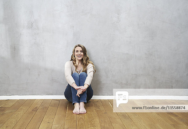 Lächelnde blonde Frau auf dem Boden vor grauer Wand sitzend