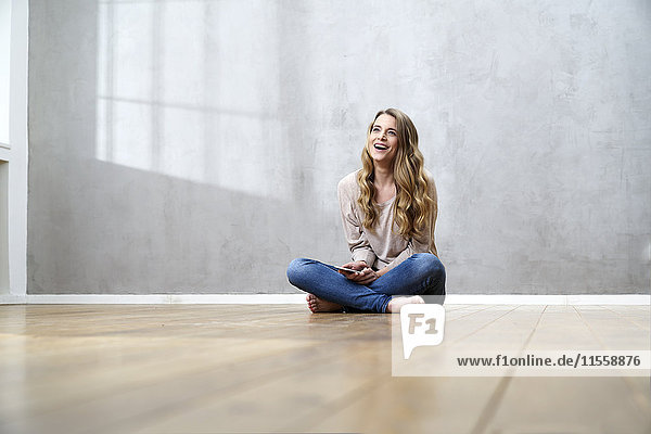 Lachende blonde Frau auf dem Boden sitzend mit Handy