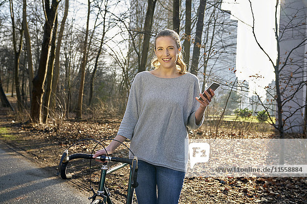 Porträt einer lächelnden blonden Frau mit Rennrad und Handy