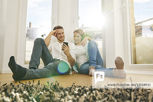 Lächelndes Paar sitzt auf dem Boden und schaut auf das Handy.