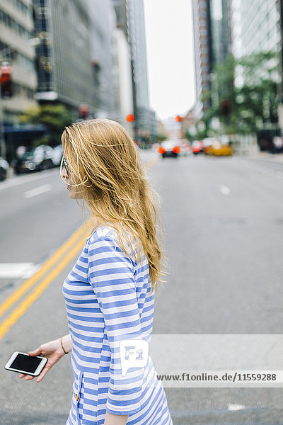 USA  New York  Manhattan  Junge Frau  die auf der Straße geht und ein Handy in der Hand hält.