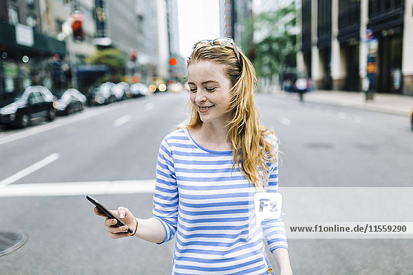 USA  New York  Manhattan  Junge Frau  die auf der Straße geht und ein Handy in der Hand hält.