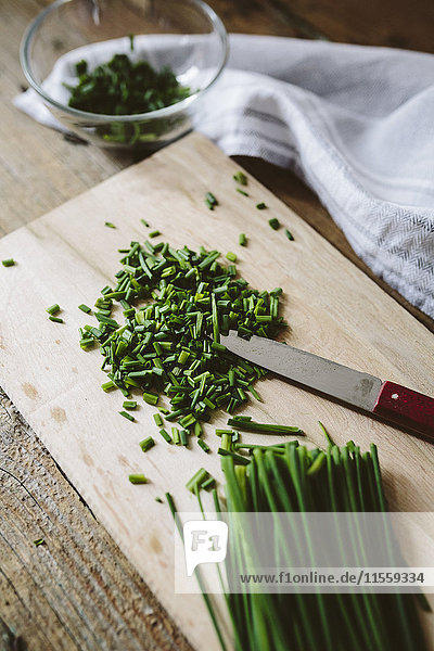 Chopped and whole chives and kitchen knife on wooden board