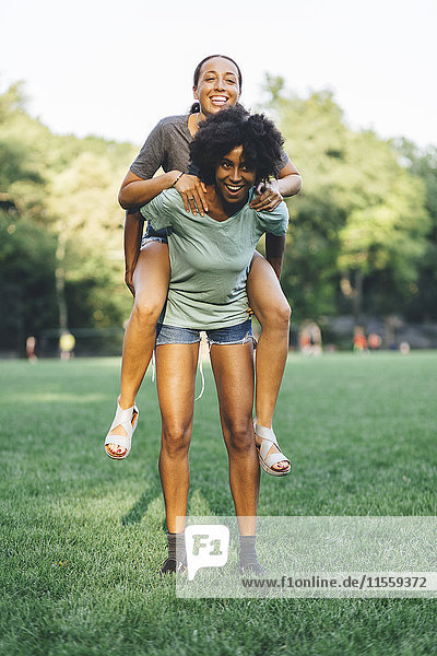 Young woman giving her friend a piggyback ride in a park