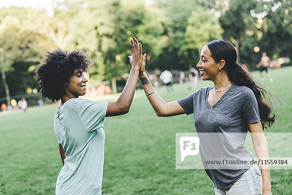 Two young woman high fiving in a park
