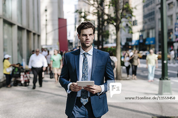 Handsome businessman walking in Manhattan  carrying digital tablet