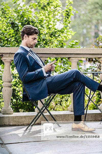 Geschäftsmann in Manhattan sitzend auf Gartenstuhl mit Smartphone