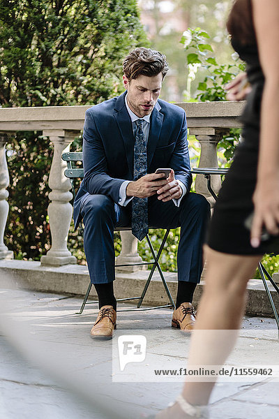 Geschäftsmann in Manhattan sitzend auf Gartenstuhl mit Smartphone