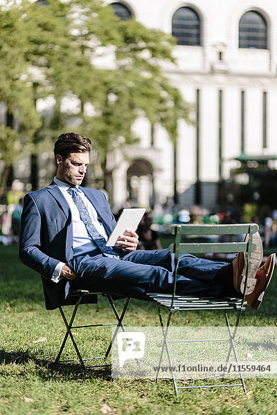 Geschäftsmann in Manhattan sitzend auf Gartenstuhl mit digitalem Tablett mit Füßen nach oben