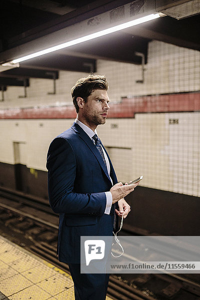 Businessman standing at a New York metro station using smart phone