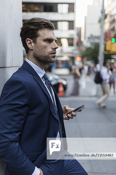 Businessman leaning on a wall in the city  using smart phone