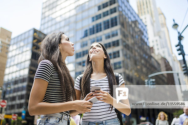 USA  New York City  zwei Zwillingsschwestern mit Mobiltelefonen in Manhattan beim Nachschlagen