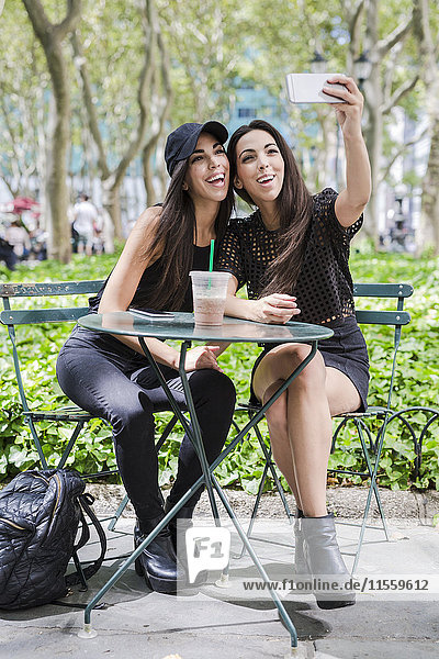 Zwei Zwillingsschwestern  die einen Selfie bei Tisch im Park nehmen.