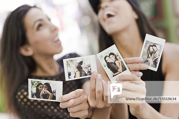 Two happy twin sisters holding instant photos of themselves